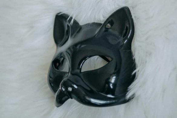 Eine Pup Play-Maske in Schwarz liegt auf einem flauschigen weißen Untergrund.