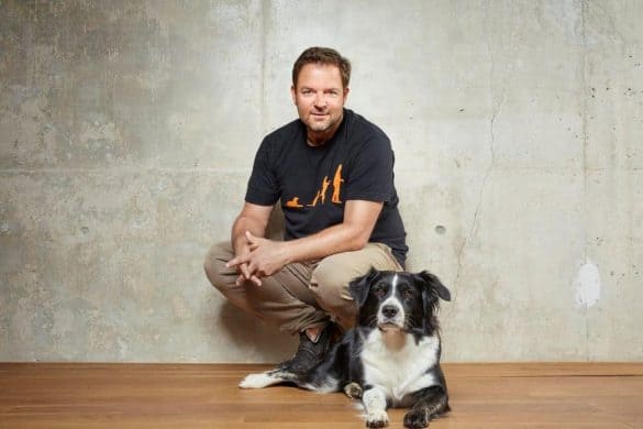 Martin Rütter kniet und vor ihm liegt ein Hund am Boden.