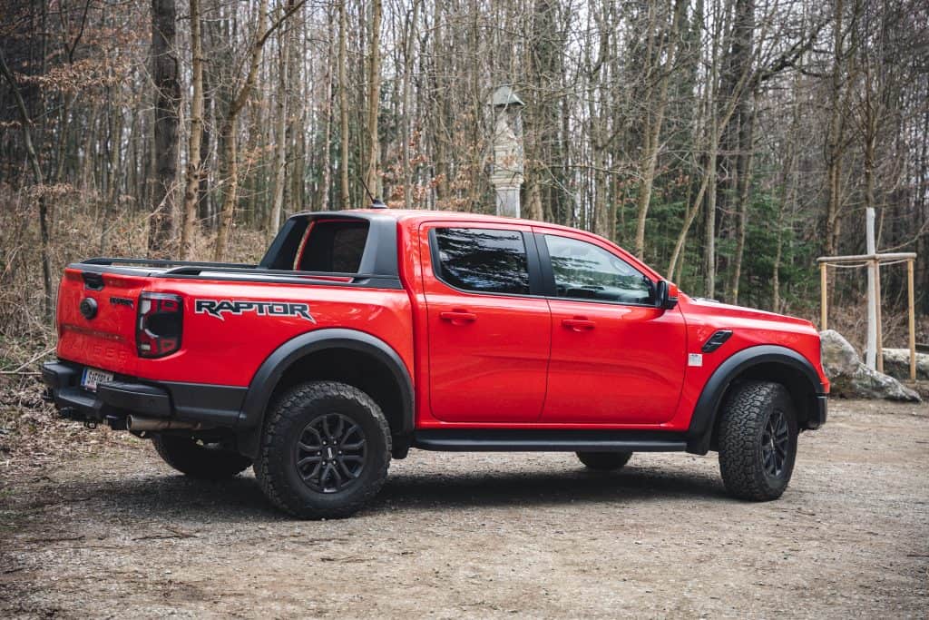 Der Ford Ranger Raptor® in Rot von der Seite, mit Wald im Hintergrund.